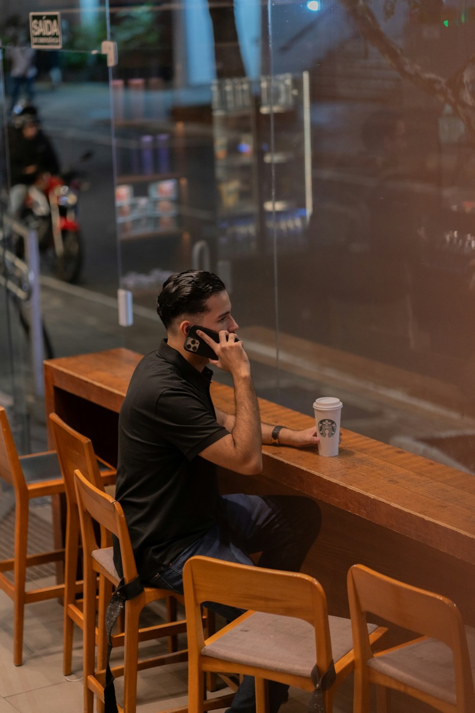 Homem sentado no balcão de uma cafeteria falando ao telefone